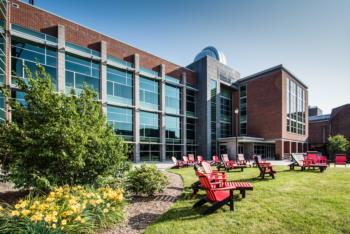 science building with red chairs & blooming flowers