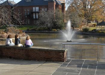 three people sitting by a pond with a fountain