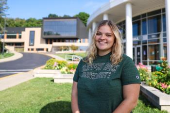 student smiling in front of campus building