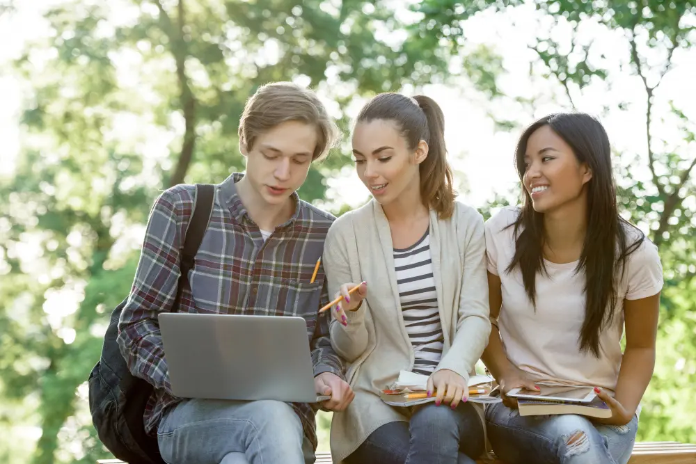 three students studying with laptop talking